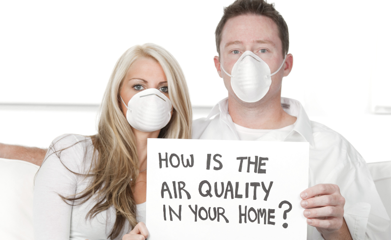 Two people with masks holding a sign that says how is the air quality in your home? Referencing indoor air quality.